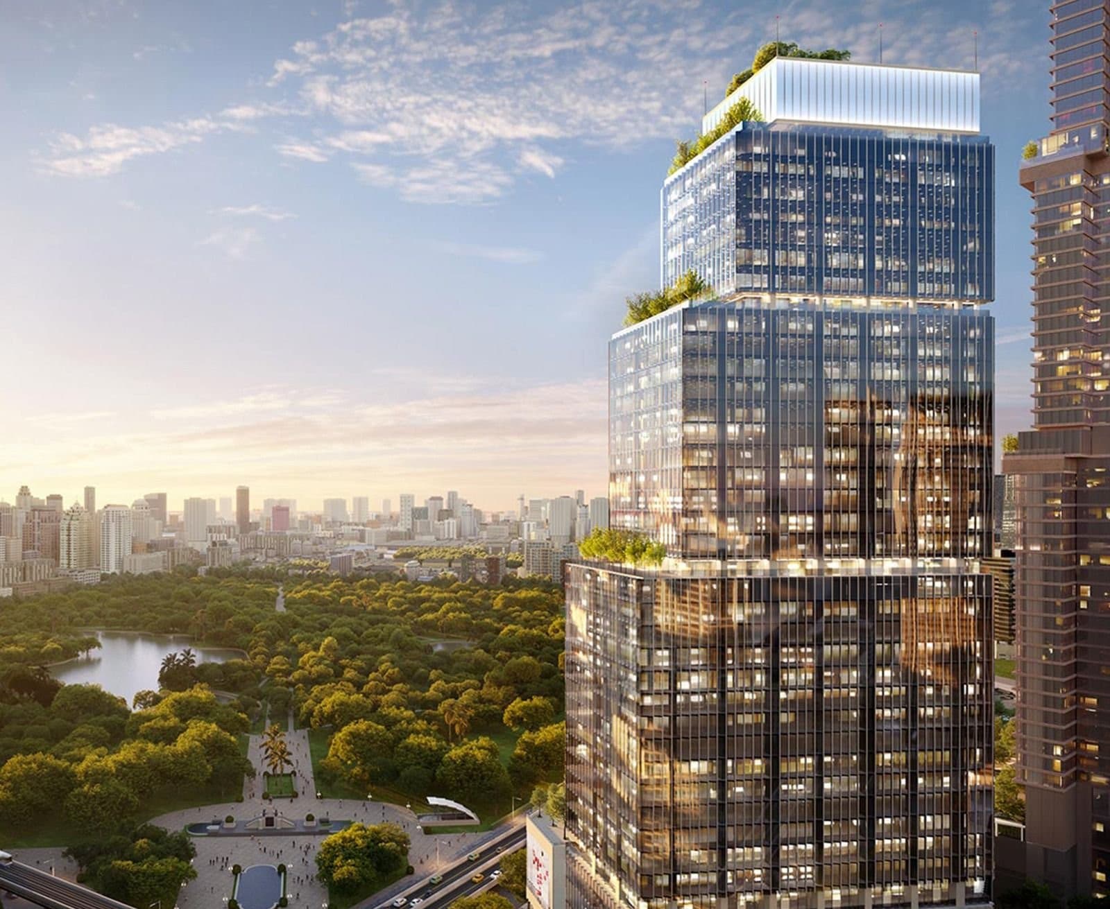 Glass building with lush green park in the back and city skyline on the horizon.